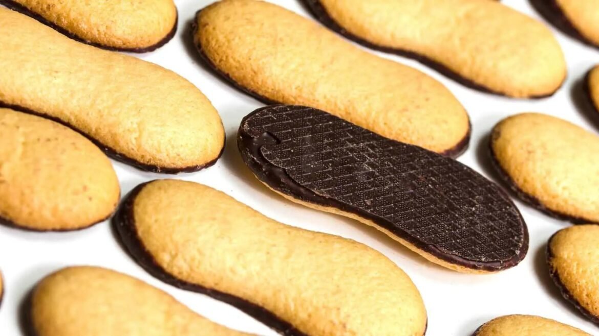 Row of golden oval cookies on a white surface, with one dark chocolate-covered cookie in the foreground