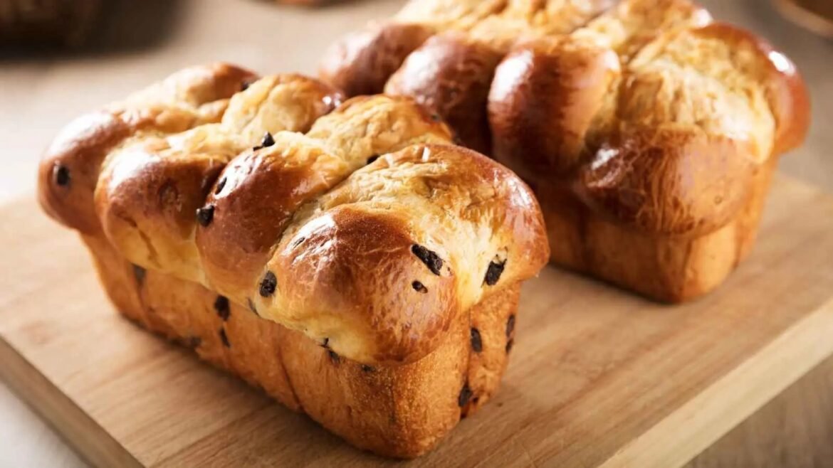 Golden braided loaves with dark chocolate chips on a wooden cutting board.