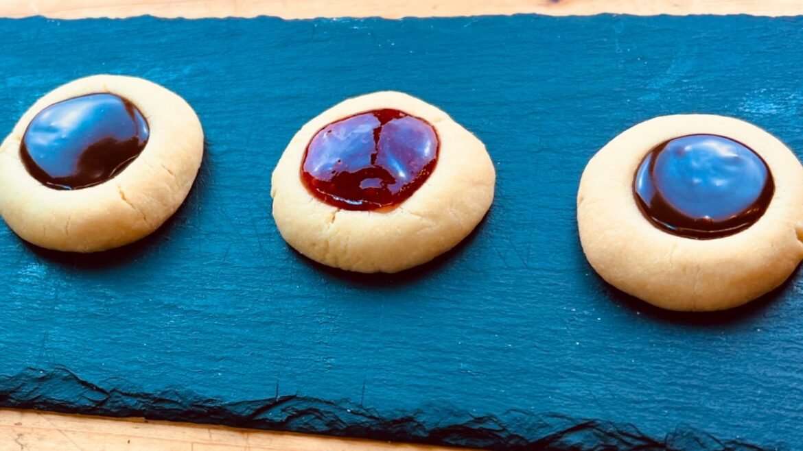 Three thumbprint cookies with glossy chocolate centers on a blue slate board.