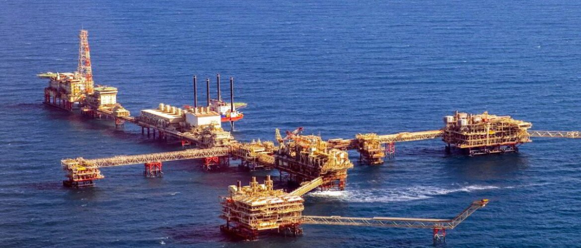 A cluster of offshore oil rigs connected by walkways on calm blue sea.