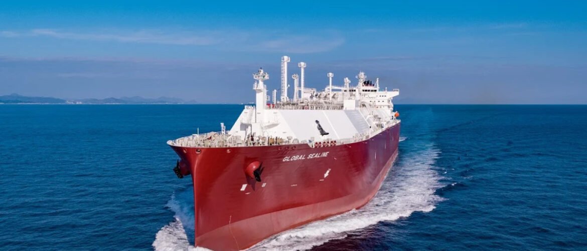 Red and white bulk carrier sailing through calm blue ocean with a white wake behind it, viewed from above