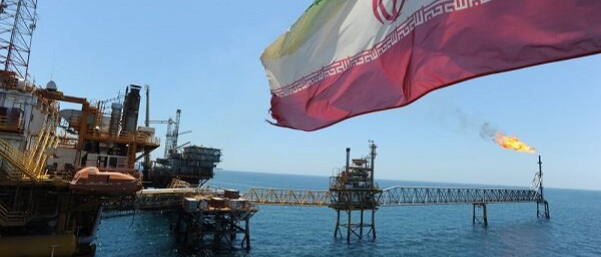 Offshore oil platform with a gas flare in the distance; an Iranian flag waves in the foreground.