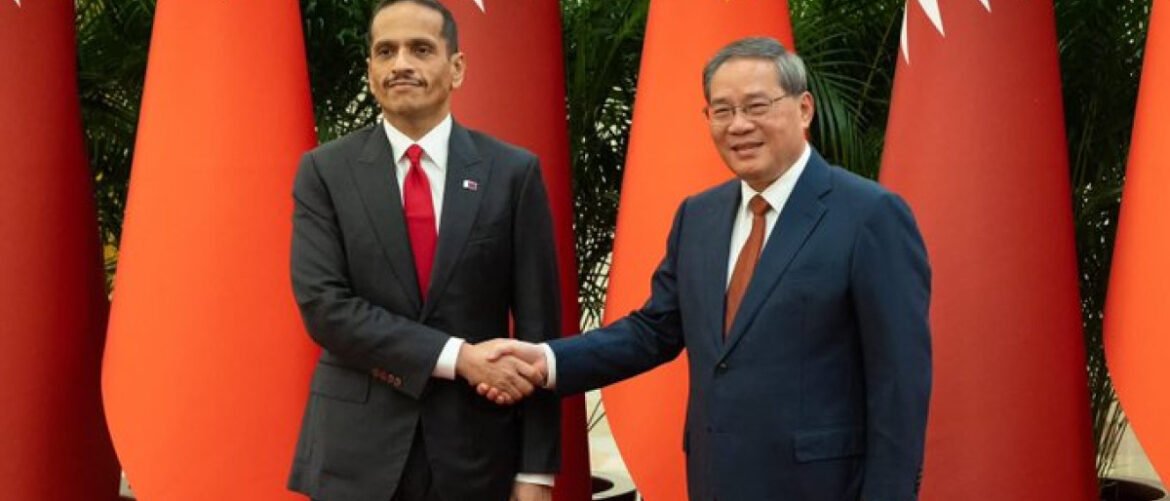 Two men in suits shake hands in front of large orange decorative columns at a formal event.
