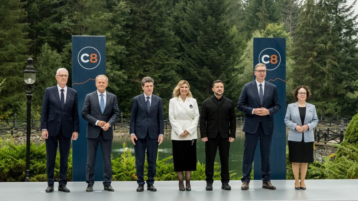 Seven professionals in formal attire pose outdoors between two blue C8 banners at a ceremonial event.