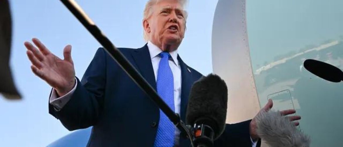 Public figure speaking outdoors with multiple microphones, an airplane fuselage visible in the background.