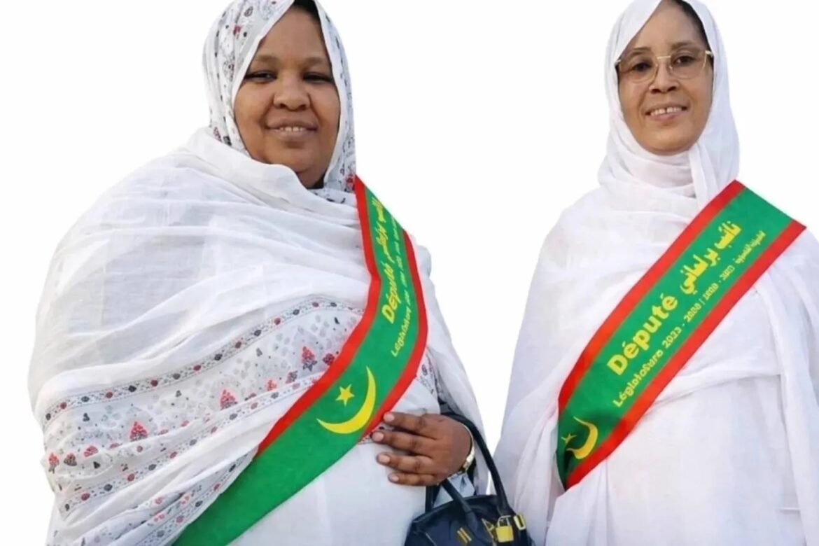 Two women in white clothing wear green sashes with red borders reading 'Député'—posing for a campaign photo.